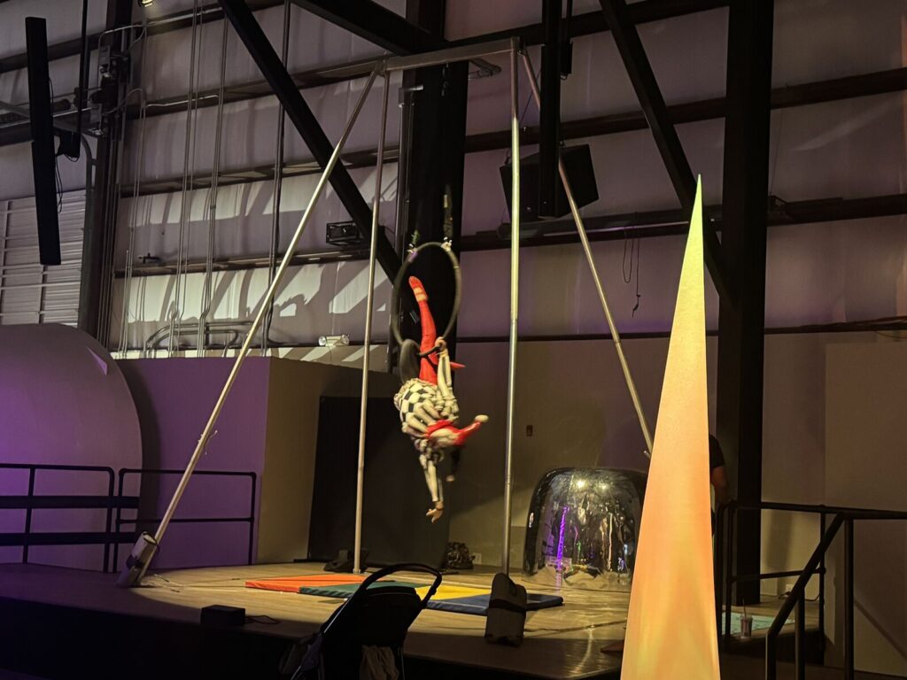 An aerialist in a checkered costume performing upside down on an aerial hoop
