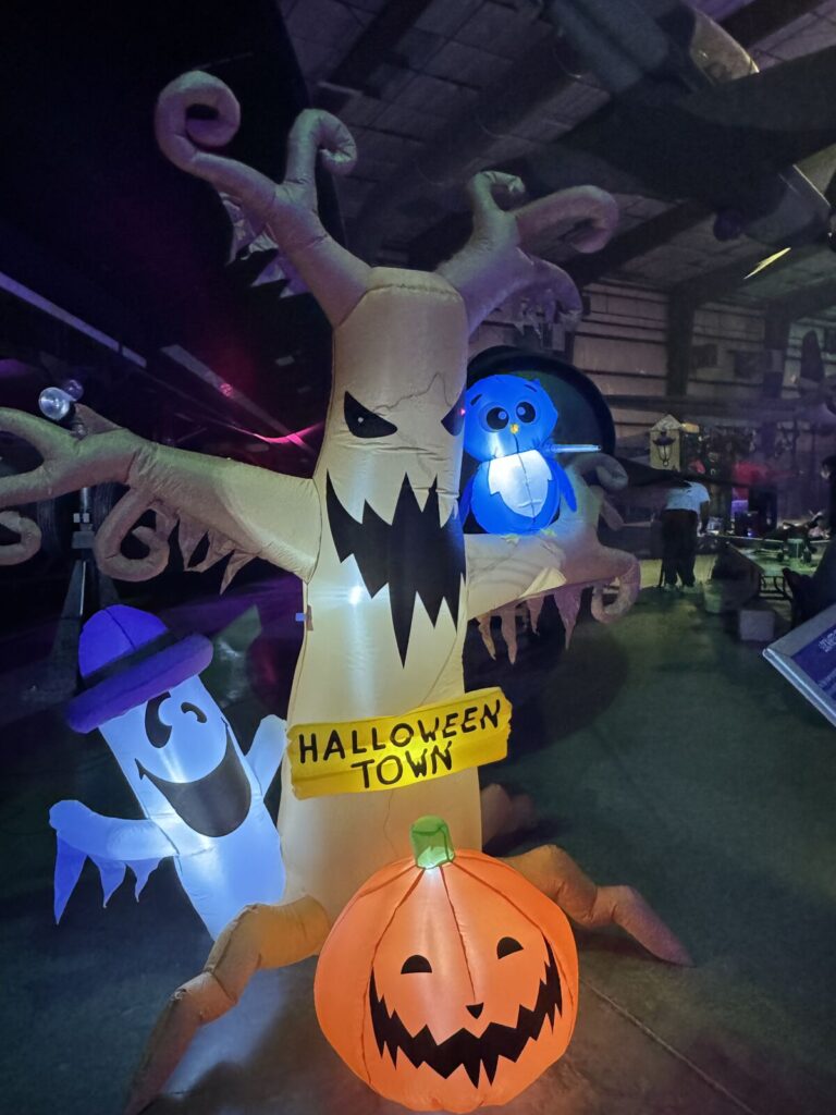 An inflatable haunted tree with a Halloween Town sign, a ghost in a purple hat, a blue owl and a jack-o'-lantern