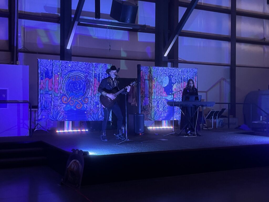 A guitarist in a cowboy hat and a keyboard player performing on a stage lit in blue